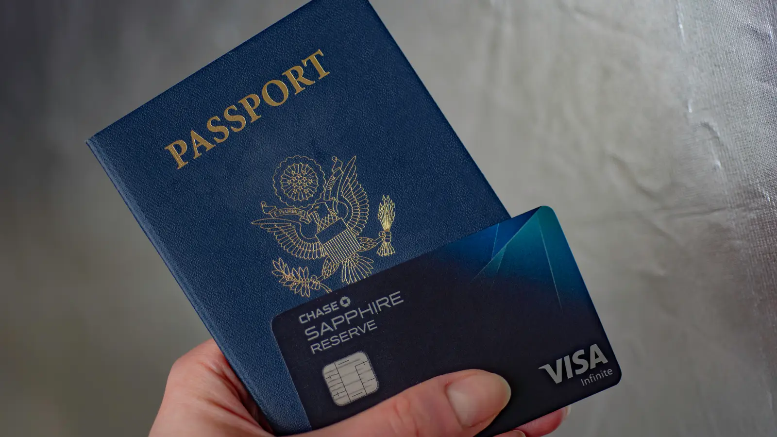 A U.S. passport sitting on a table next to a credit card and a smartphone showing a banking app login screen, in a well-lit home setting