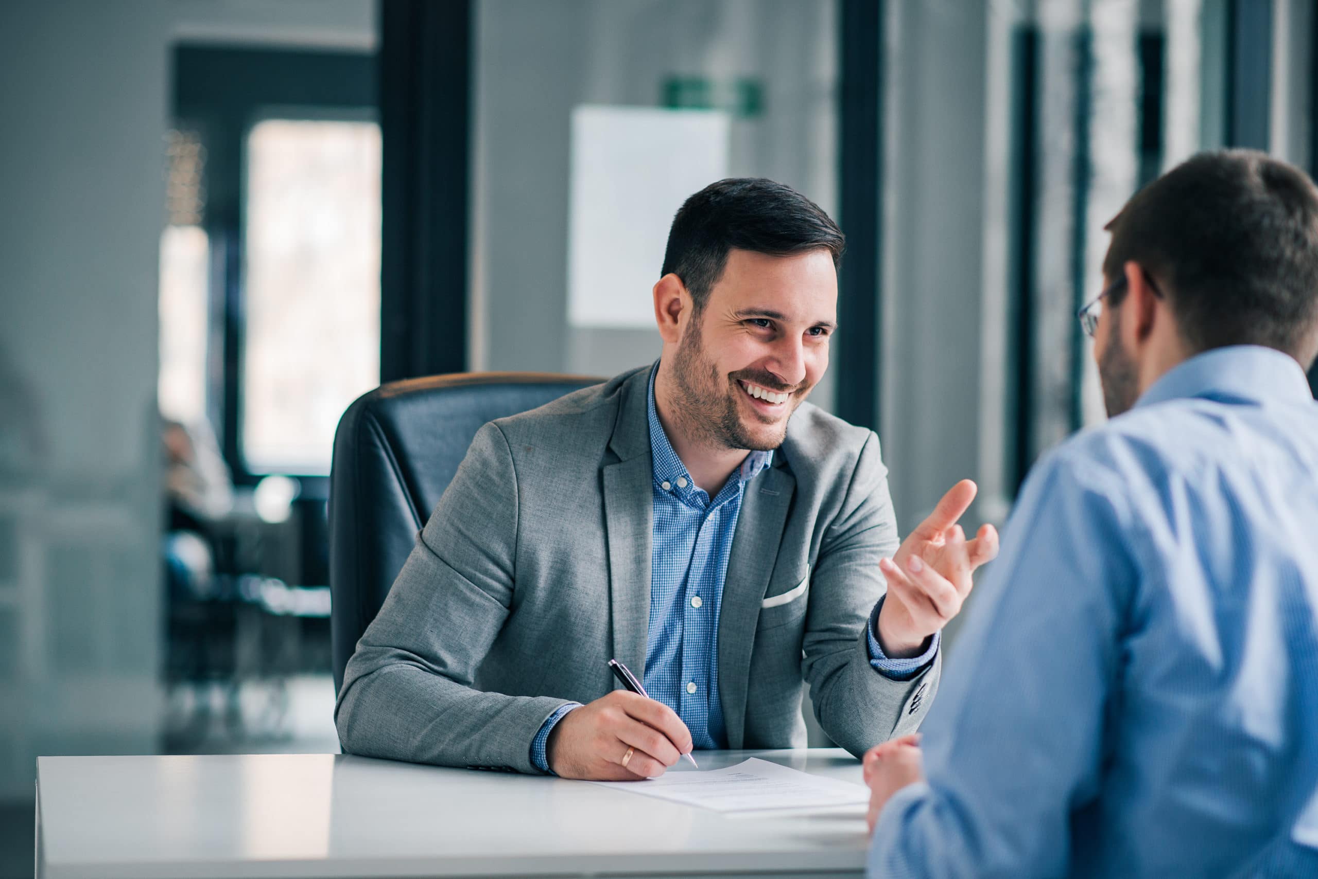 A mortgage loan officer seated at a desk speaking with a couple across the table while reviewing application paperwork