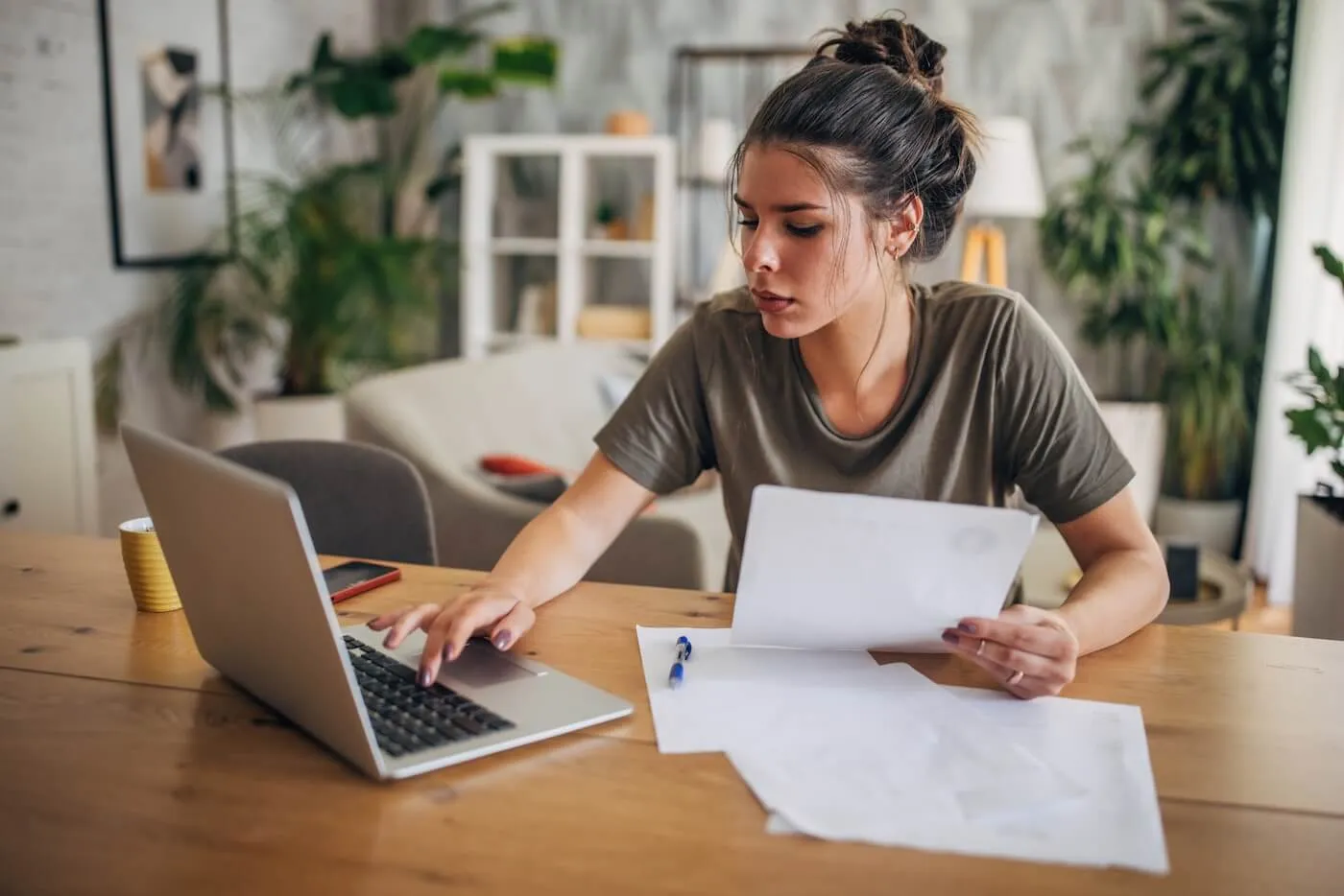 A person at a kitchen table reviewing printed credit report pages with a highlighter and a laptop nearby
