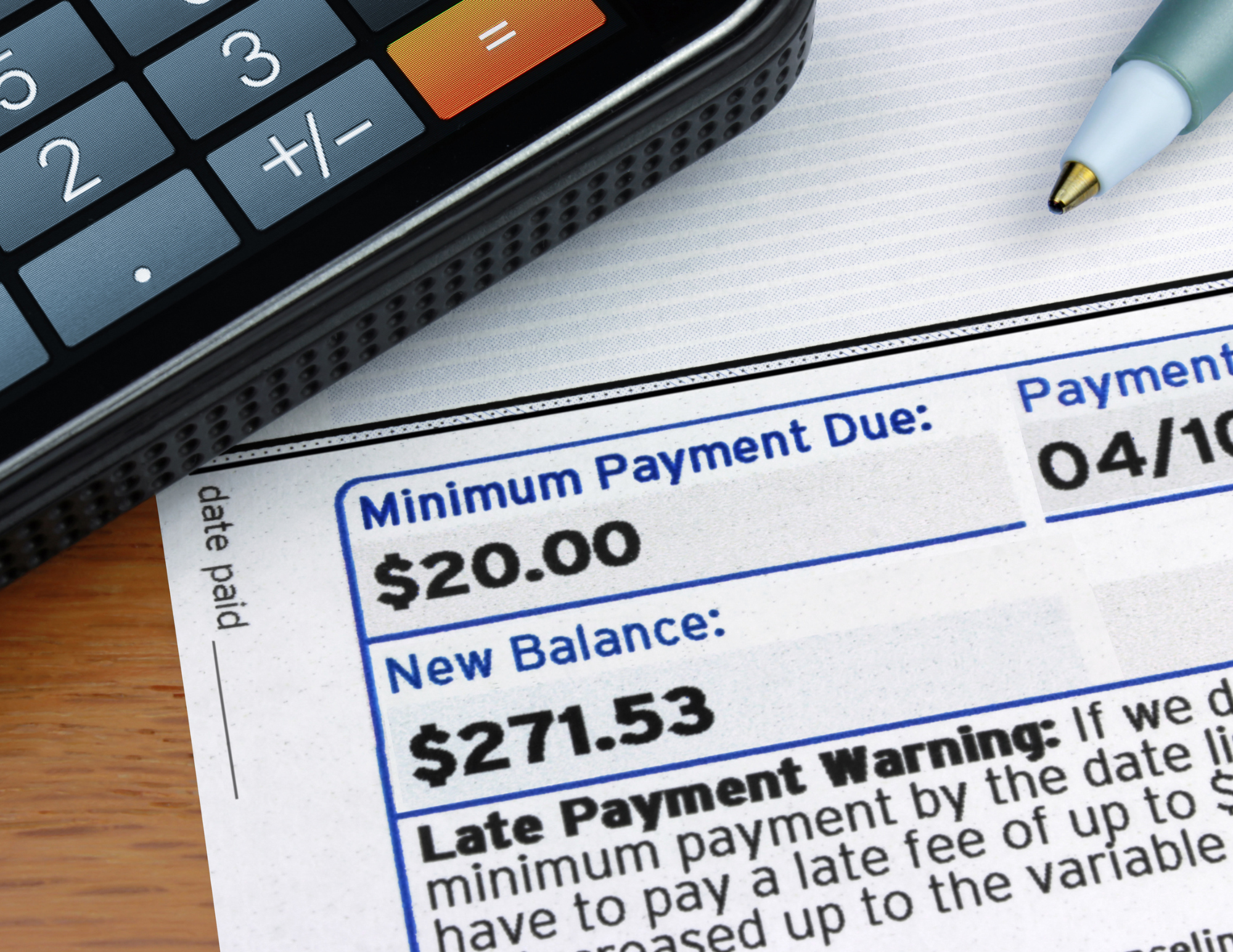 A person sitting at a kitchen table reviewing a credit application and monthly bills, with a calculator and a laptop open